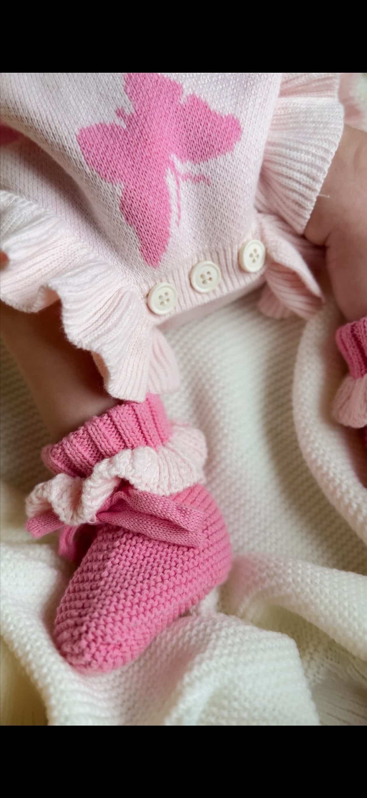 Pink baby booties and socks with a matching outfit on a white background