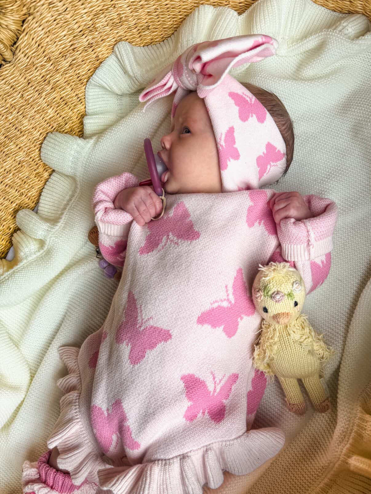 Newborn baby wrapped in a pink butterfly-patterned blanket with a plush toy, lying on a textured surface.