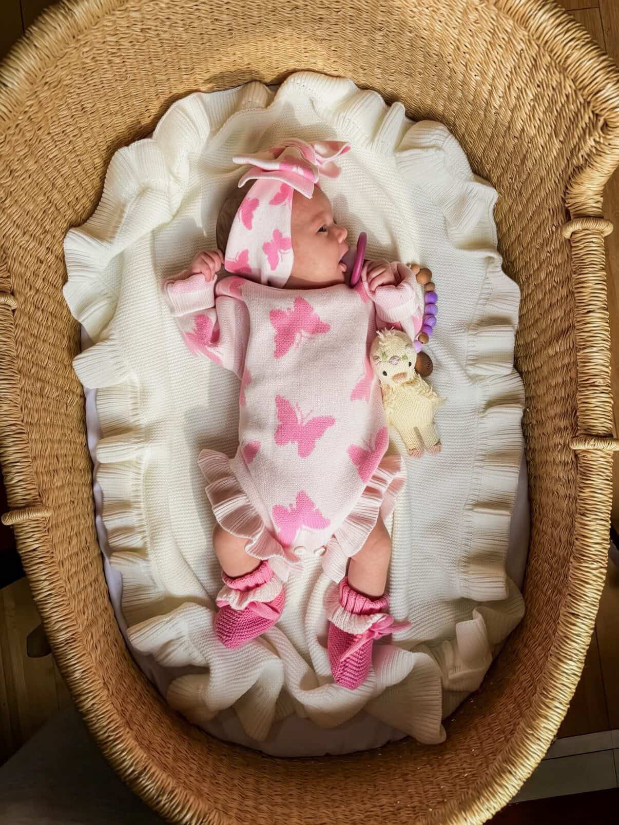 Newborn baby in a pink butterfly outfit lying in a wicker crib.