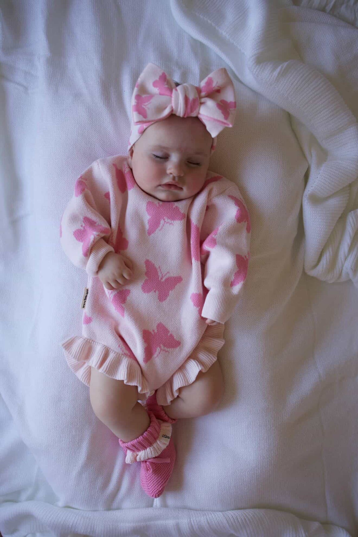 Baby in pink butterfly onesie with matching headband and socks on a white blanket