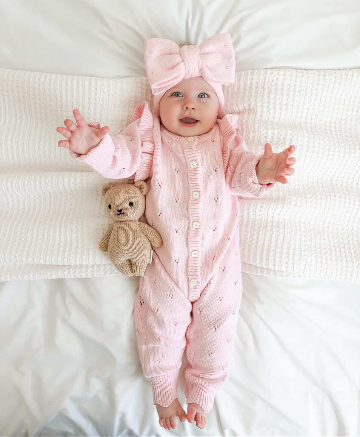 Baby in a pink outfit with a bow headband lying on a white blanket