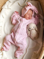 Newborn baby in pink outfit with bunny ears and plush toy in a crib