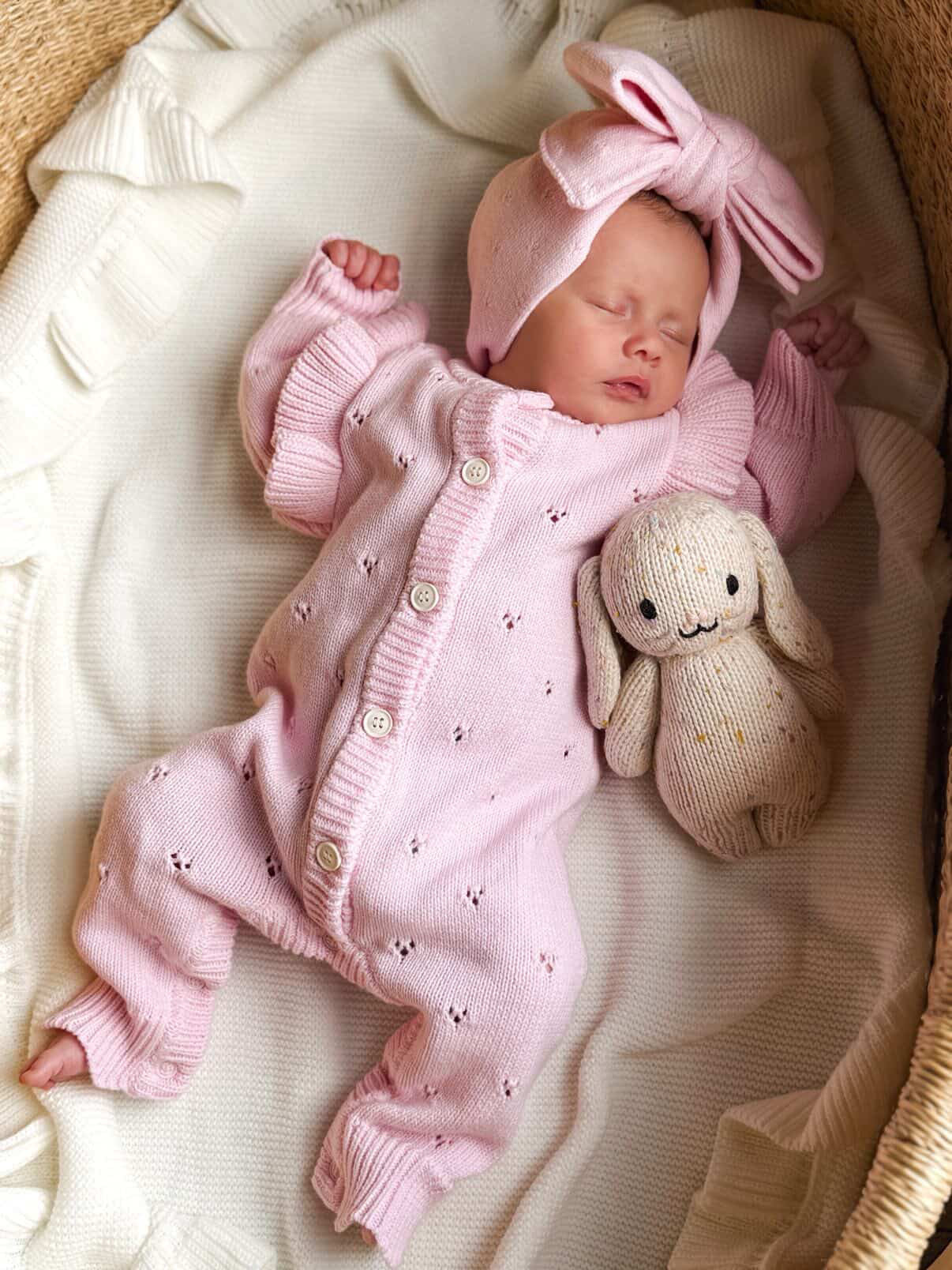 Newborn baby in pink outfit with bunny ears and plush toy in a crib