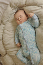 Baby in a patterned onesie lying on a beige cushion