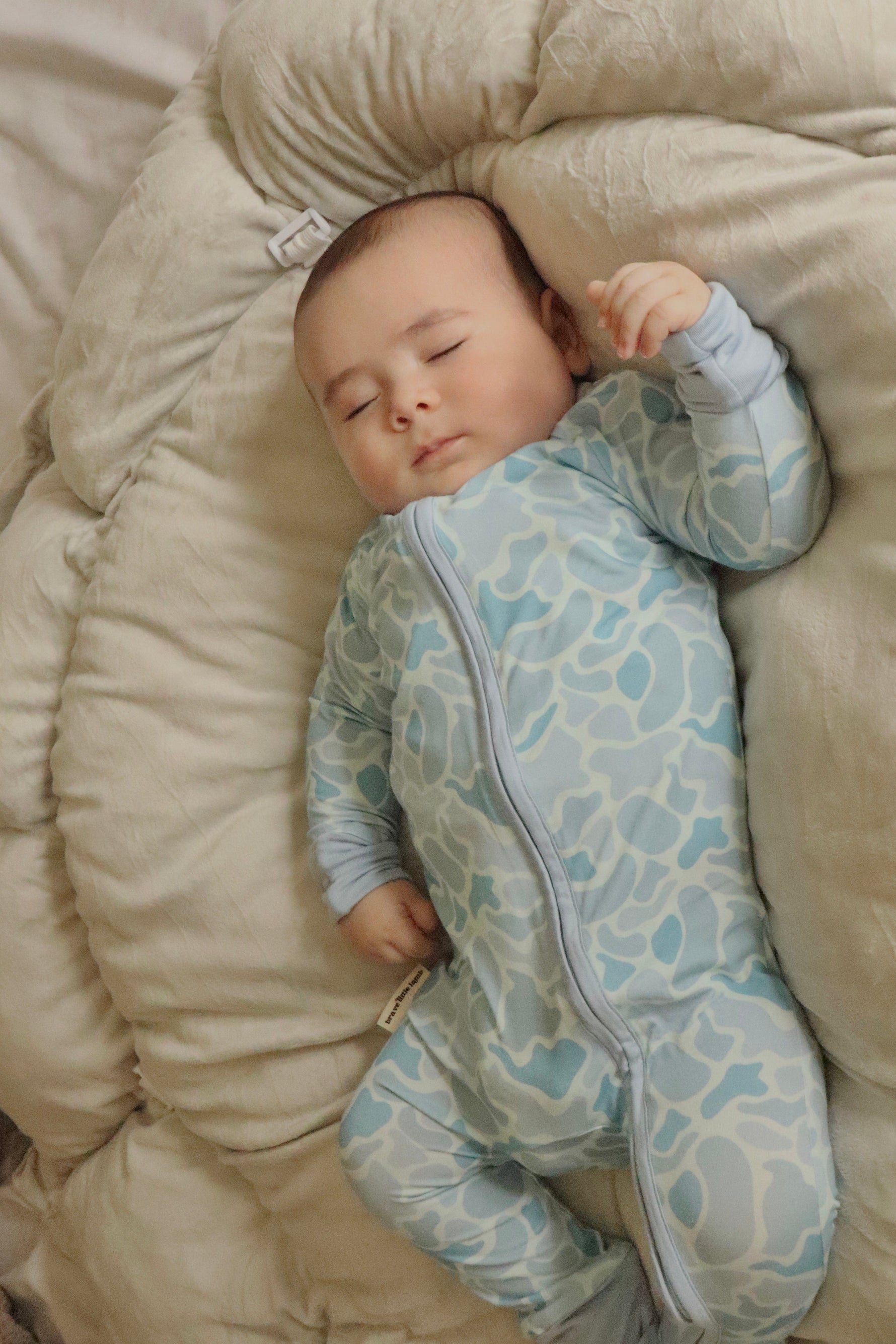 Baby in a patterned onesie lying on a beige cushion
