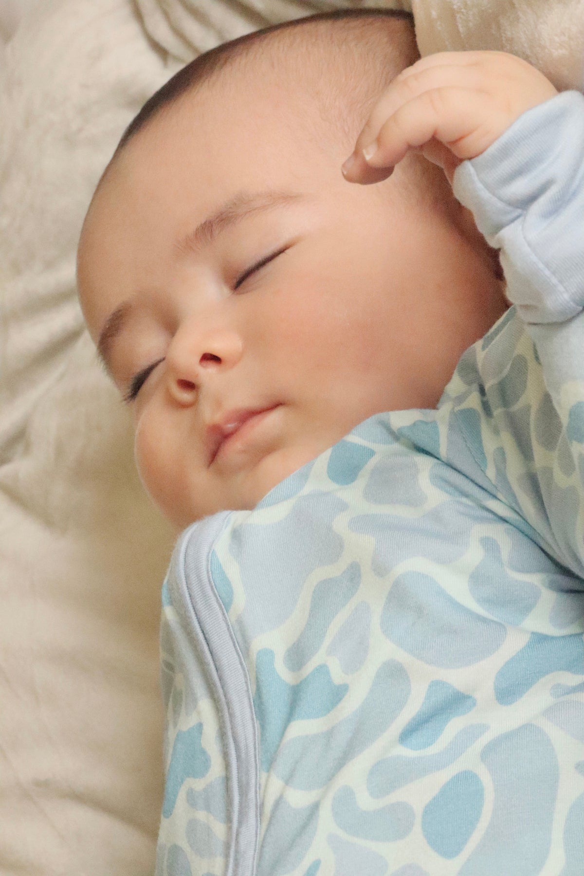 Baby sleeping peacefully wearing a blue and white patterned outfit.