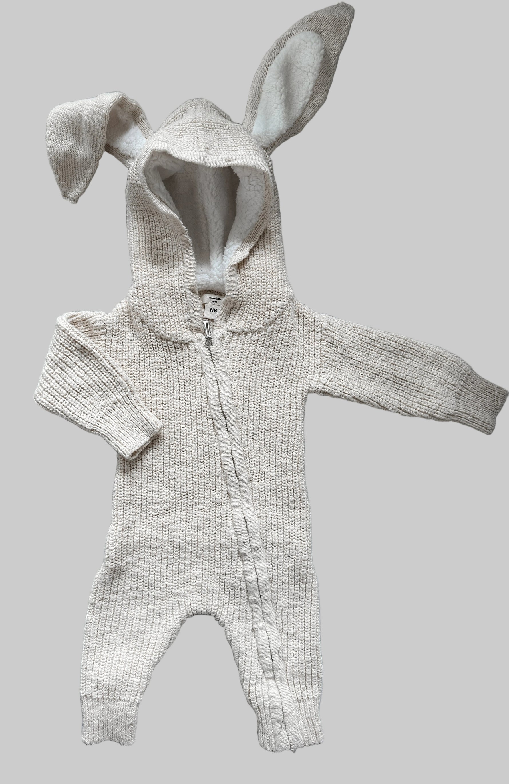 Knitted baby romper with bunny ears on a gray surface
