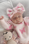 Newborn baby in pink butterfly outfit with matching headband, surrounded by soft textures.