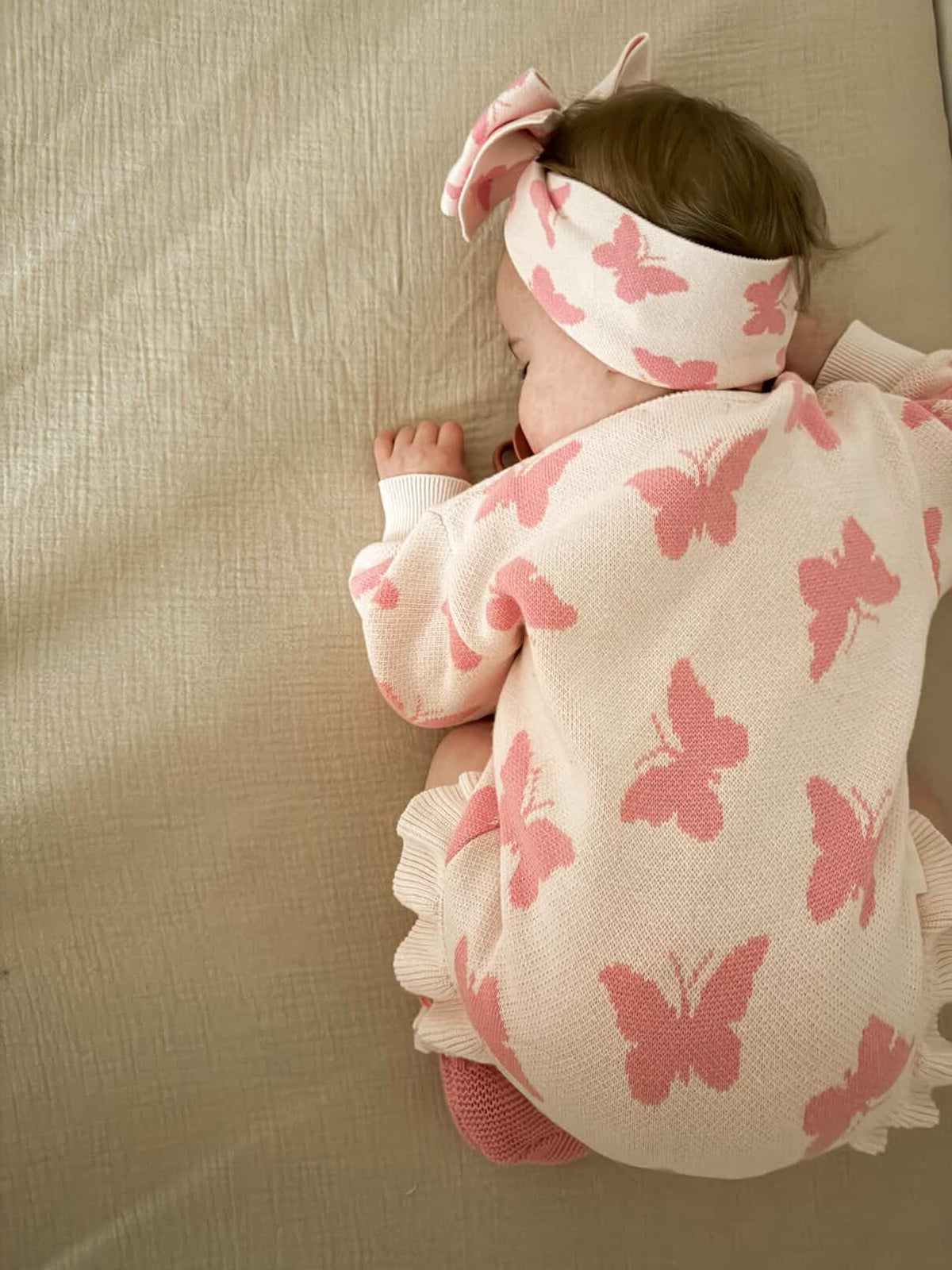 Baby wearing a pink butterfly-patterned outfit and headband on a beige surface