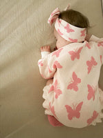 Baby wearing a pink butterfly-patterned outfit and headband on a beige surface