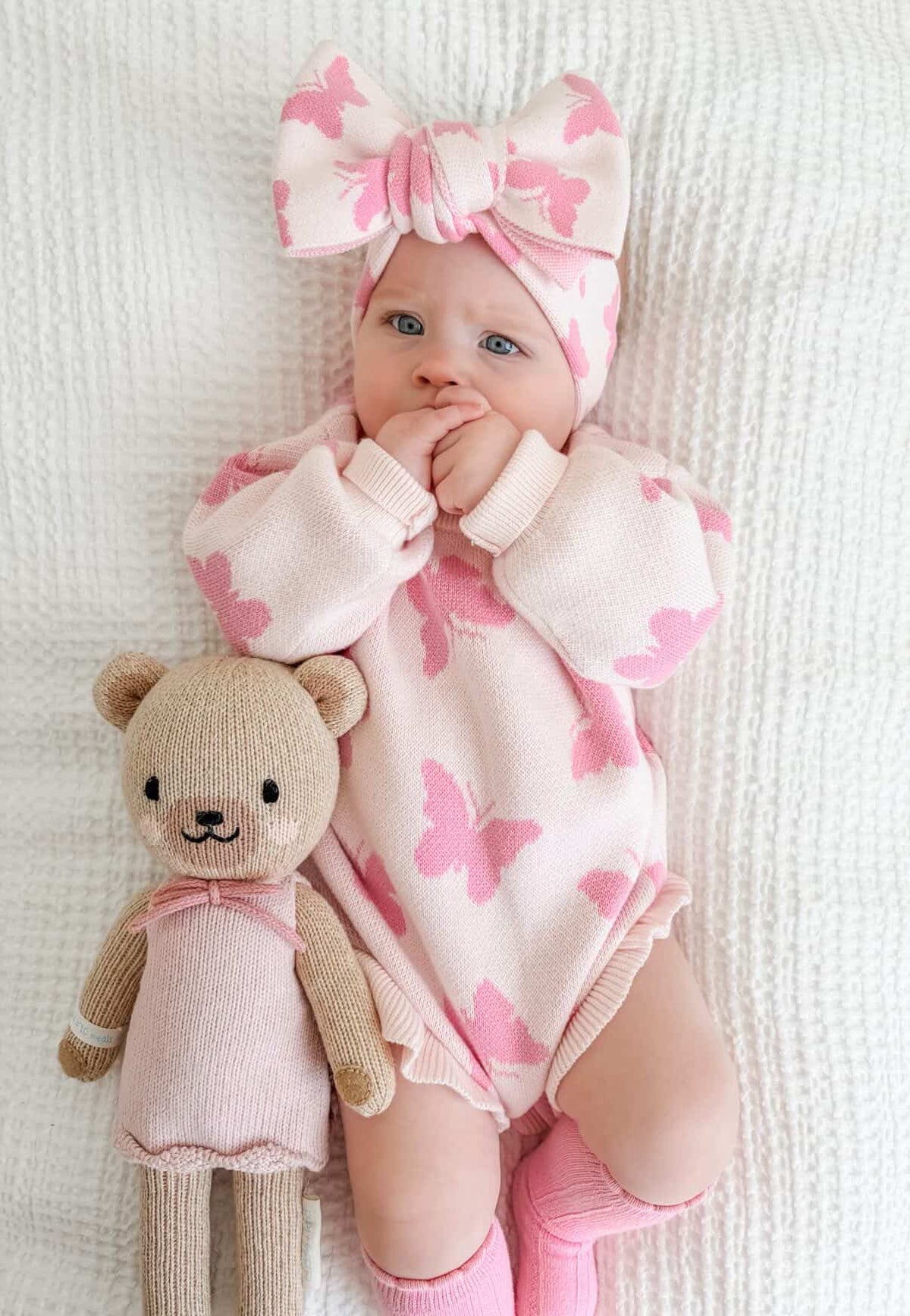 Baby in pink butterfly outfit with a teddy bear on a white background