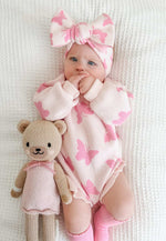 Baby in pink butterfly outfit with a teddy bear on a white background