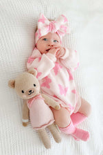 Baby in pink floral outfit with teddy bear toy on white blanket