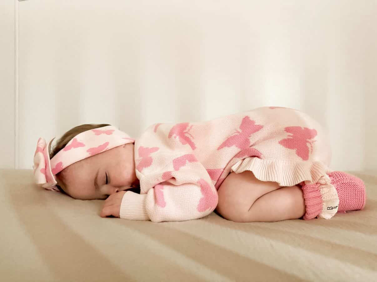 Baby in pink floral outfit sleeping on a beige surface