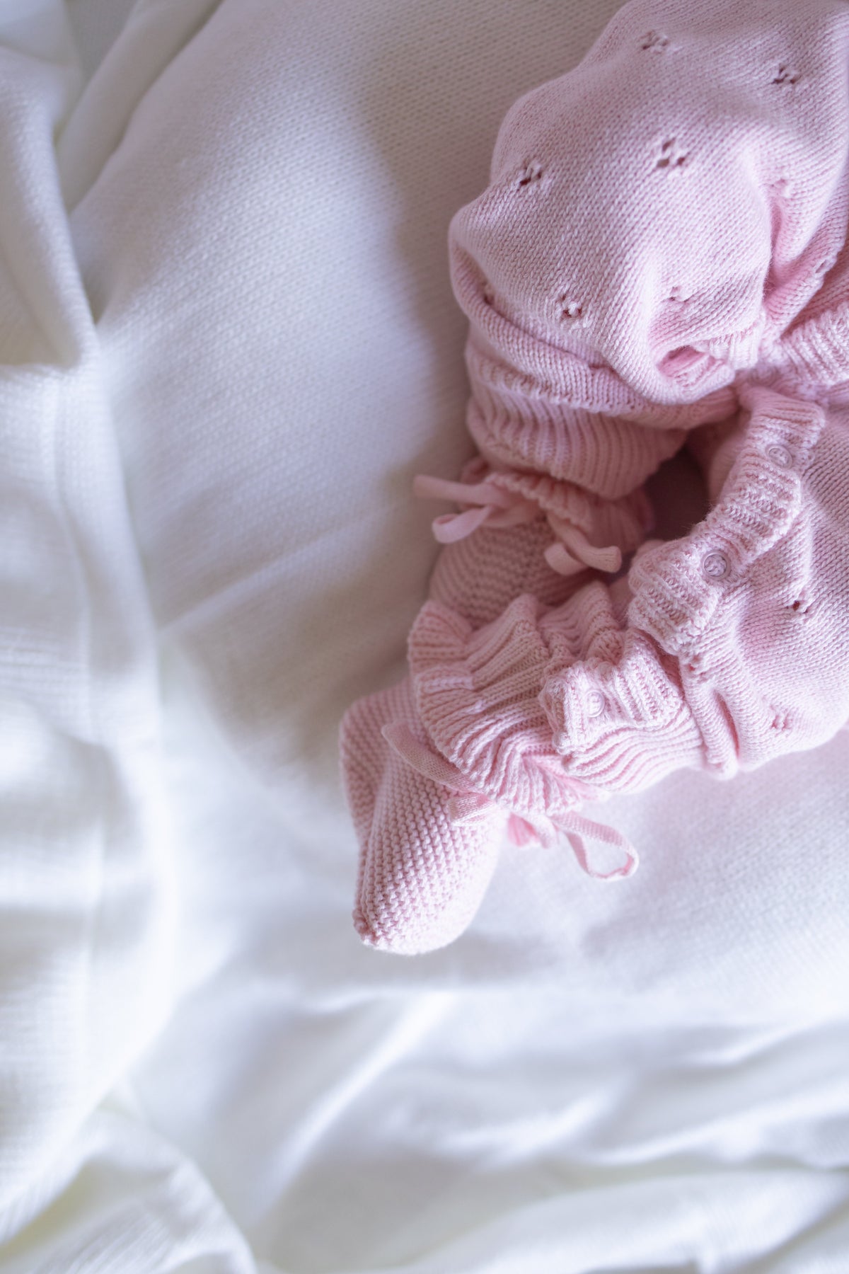 Pink knitted baby booties on a white fabric background
