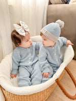 Two babies in matching blue outfits sitting in a basket.