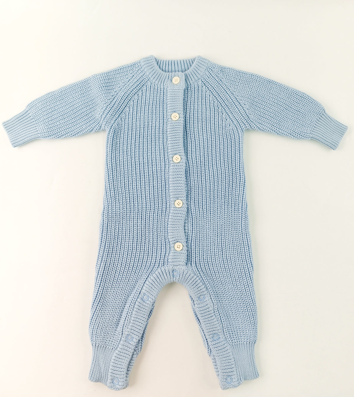 Blue knitted baby romper on a light beige background