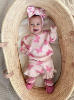 Baby in a pink butterfly outfit with a large bow in a woven basket