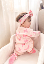 Baby in pink butterfly outfit sitting on a white chair with white curtains in the background