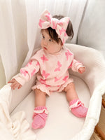 Baby in pink outfit with butterfly patterns sitting on a white surface