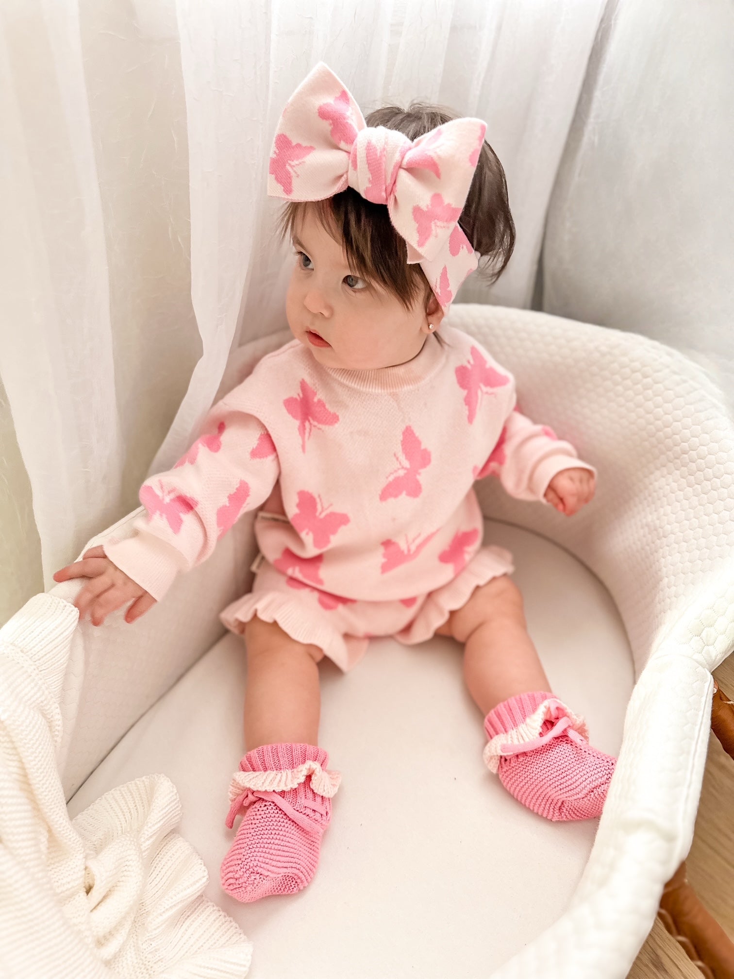 Baby in pink outfit with butterfly patterns sitting on a white surface