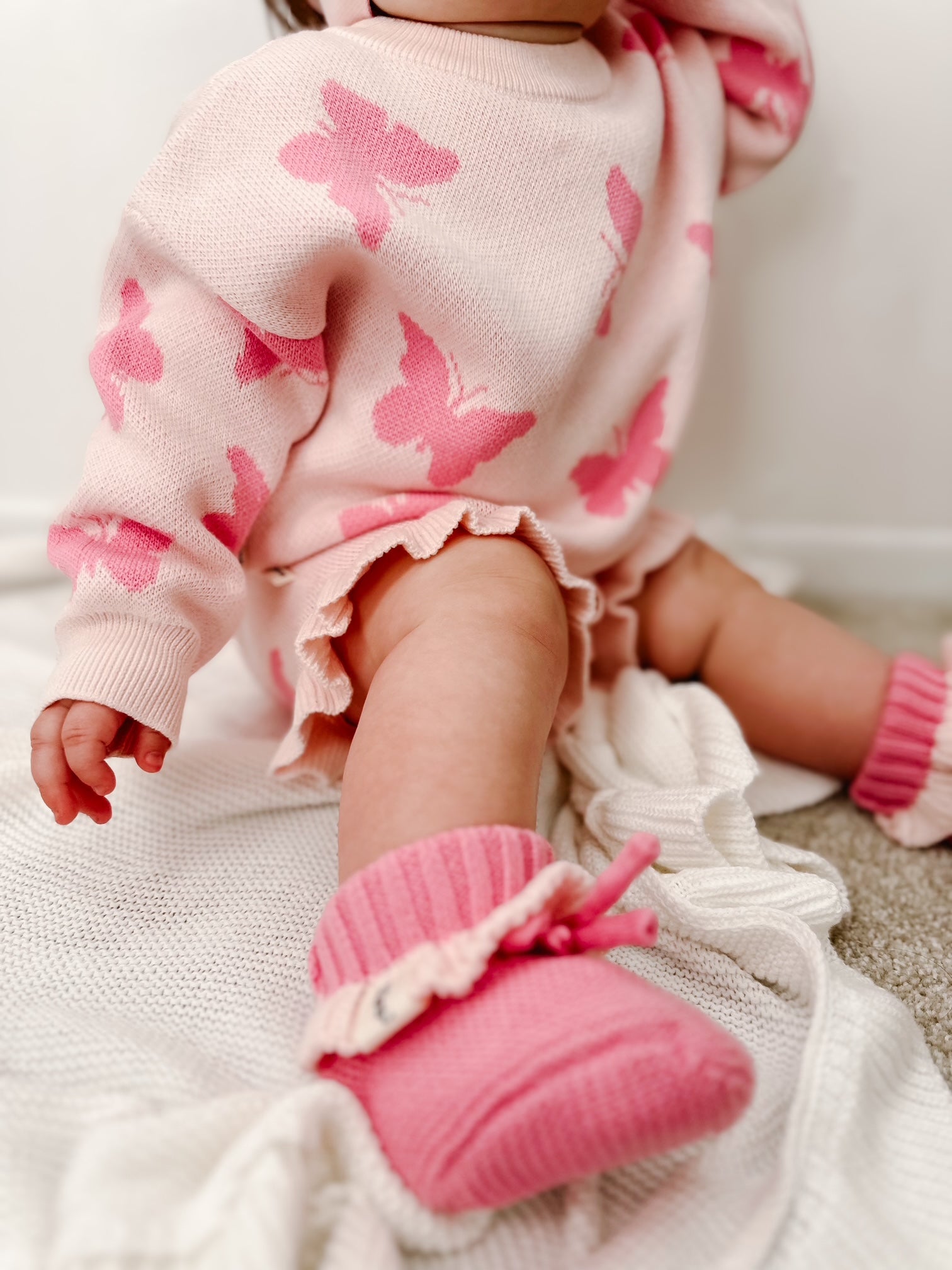 Baby in pink outfit with butterfly pattern and matching booties on a neutral background