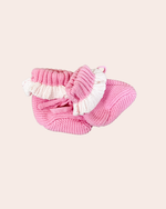 Pink knitted baby booties with white tassels on a light pink background