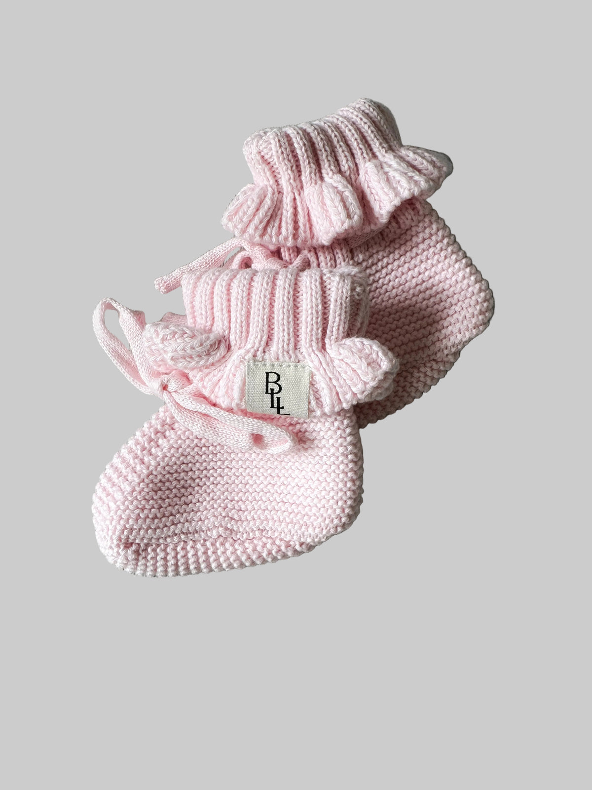 Pair of pink knitted baby booties on a gray surface