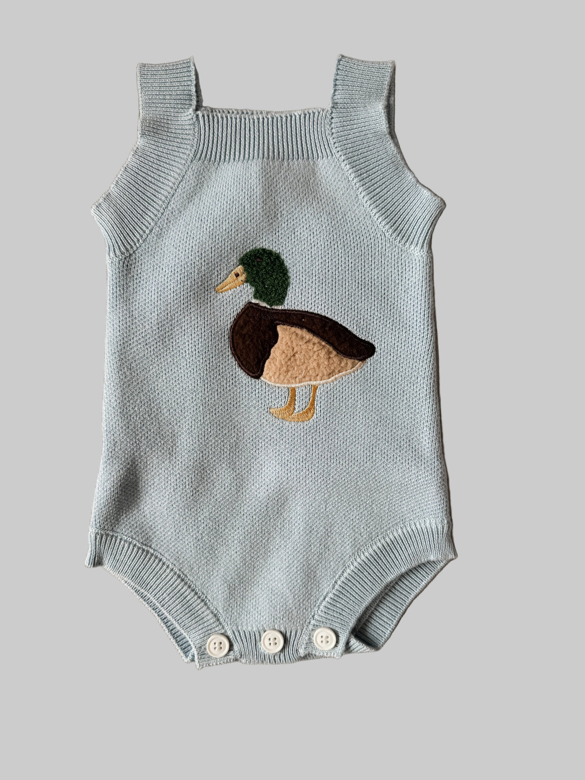 Knitted baby romper with duck design on a beige background
