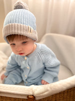 Baby wearing a blue knit hat and cardigan sitting in a basket.