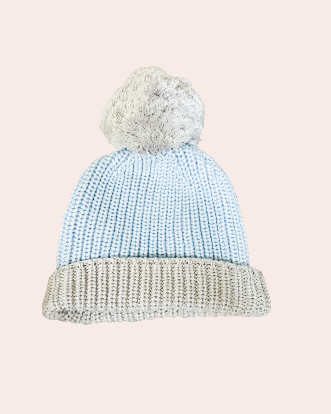 Knitted beanie with a textured pattern and fluffy pom-pom on a light pink background
