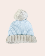 Knitted beanie with a textured pattern and fluffy pom-pom on a light pink background