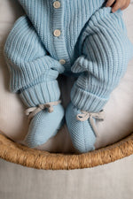 Knitted baby outfit with cardigan, pants, and booties in light blue on a white surface.