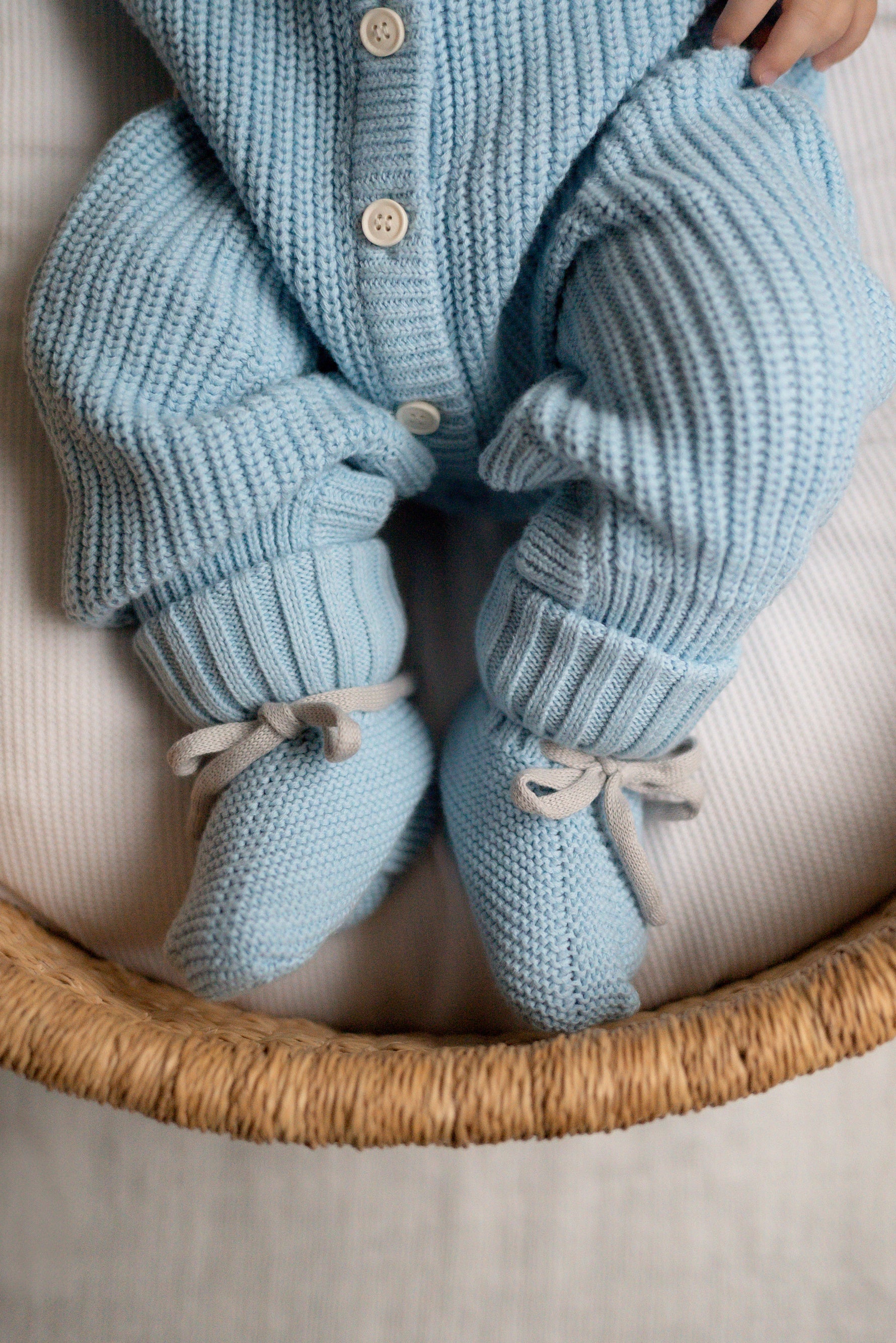 Knitted baby outfit with cardigan, pants, and booties in light blue on a white surface.