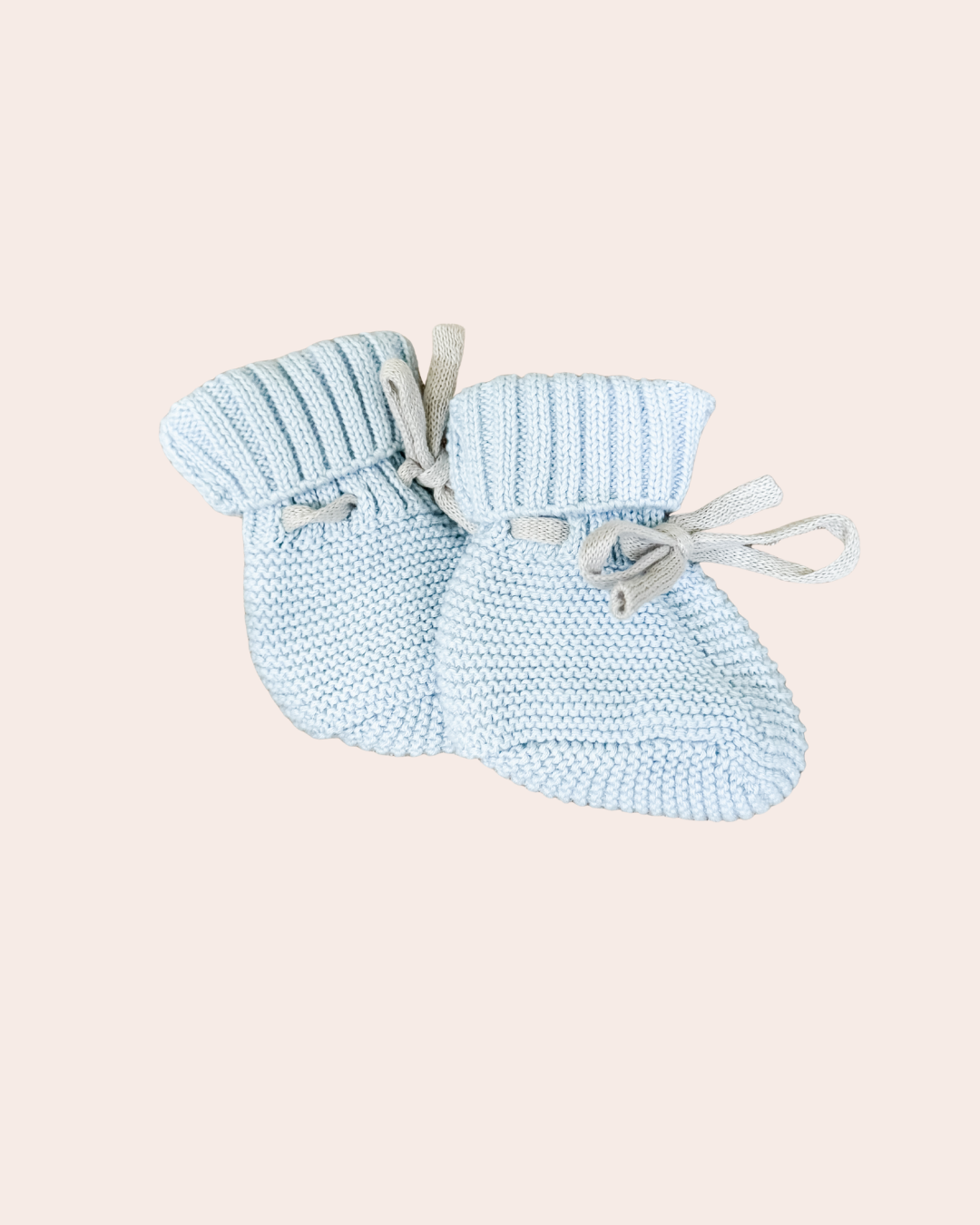 Pair of light blue knitted baby booties on a beige background