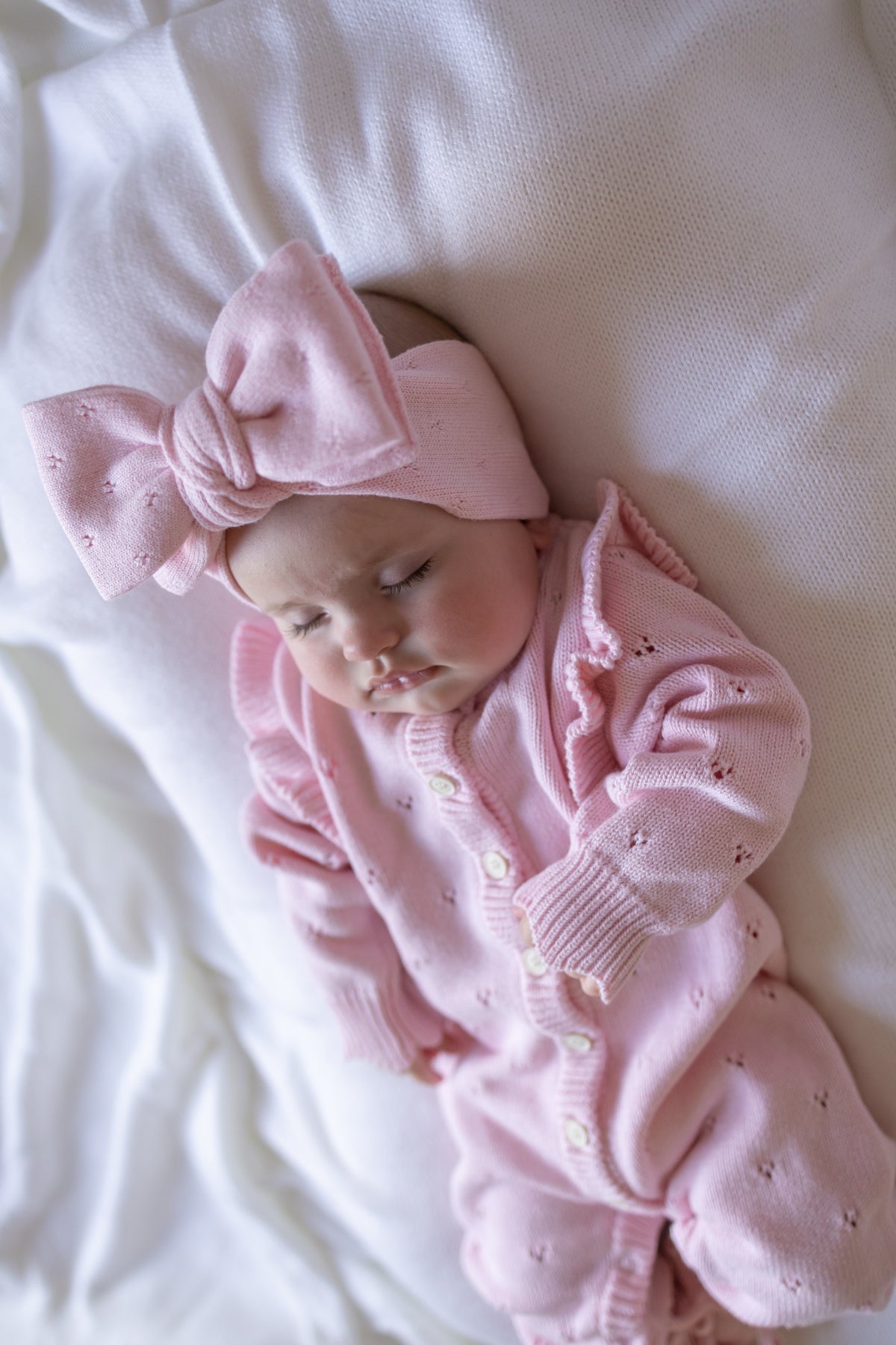 Baby in pink outfit with a large bow on a white blanket