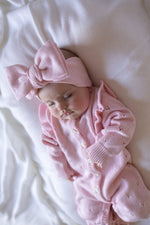 Baby in pink outfit with a large bow on a white blanket