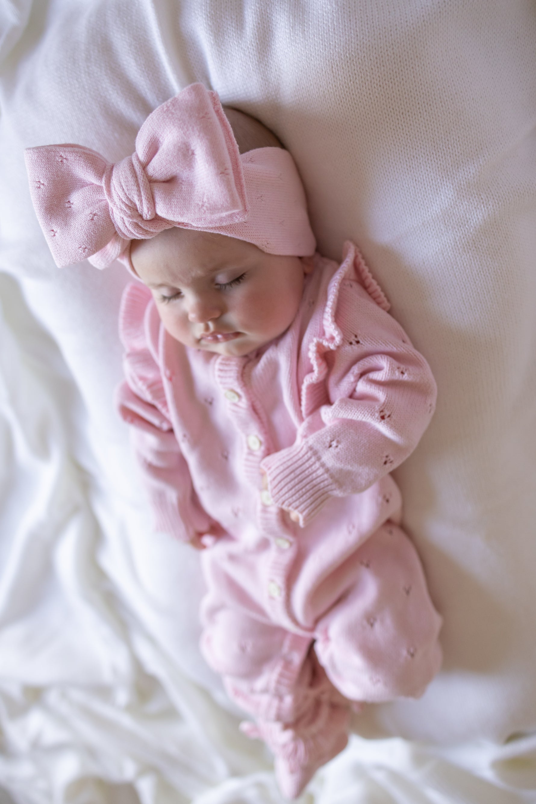 Baby in pink outfit and headband lying on a white surface